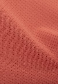 Soft, textured coral fabric with a subtle dotted pattern and slight folds creating gentle shadows and highlights.