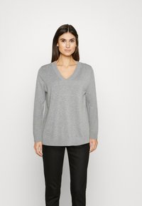 Grauer V-Ausschnitt-Pullover aus weich gestricktem Stoff mit langen Ärmeln. Verfügt über einen lockeren Schnitt und einen gerippten Saum, kombiniert mit schwarzen Hosen.