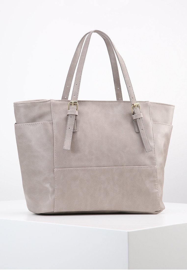 Sac cabas en cuir gris clair avec deux bretelles d'épaule ajustables, poche avant et poches latérales, présenté sur une surface blanche.