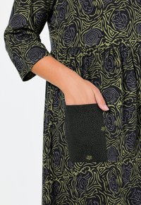 Černé šaty se zelenými vířícími vzory, s nařaseným pasem a kapsou s puntíkovaným vzorem na levém bocích. Rukávy s délkou 3/4.