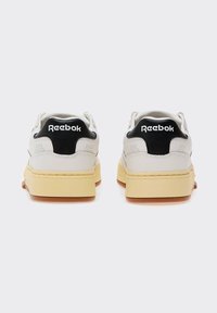 Baskets en cuir blanc avec un contrefort noir portant le logo "Reebok", une semelle intermédiaire épaisse couleur crème et une semelle extérieure en caoutchouc gomme. Design minimaliste avec perforations.