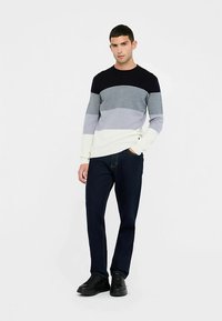 Maglione a righe in blu navy, grigio e bianco. Girocollo, maniche lunghe, texture a maglia. Abbinato a jeans scuri e sneakers nere.