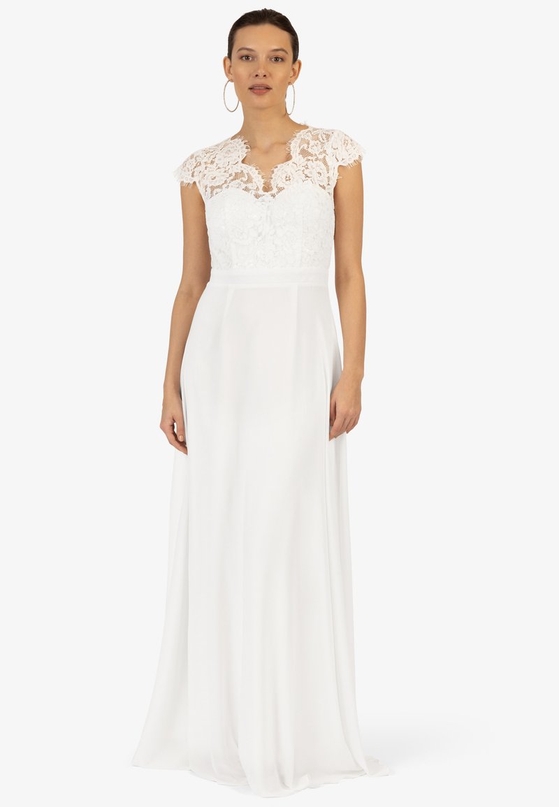 Hvid kjole med blondeoverdel og cap sleeves, flydende skørt og en tætsiddende talje, hvilket skaber en elegant silhuet.