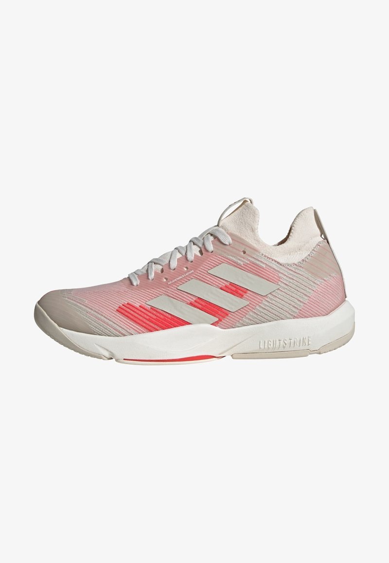 Zapatilla deportiva de color rosa claro con parte superior texturizada, cordones blancos y tres rayas grises. Presenta un acento rojo y una suela acolchada.