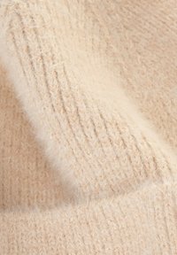 Tela de punto beige con una textura suave y esponjosa. Presenta líneas visibles del patrón de tejido que añaden profundidad y dimensión.