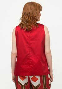 Top rosso senza maniche con una texture liscia e una cucitura centrale sul retro, abbinato a pantaloni a vita alta con motivo a forme geometriche.
