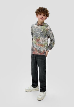 Un sweat à capuche avec un imprimé abstrait multicolore, associé à un jean en denim foncé et des baskets blanches. Le tissu semble doux et décontracté.