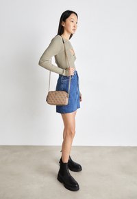 Beige ribbet langærmet top, denim miniskørt og sorte ankelstøvler. Holder en lille mønstret håndtaske med kædehank.