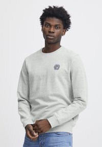 Lichtgrijze sweatshirt met een ronde hals, ribgebreide manchetten en zoom. Voorzien van een klein geborduurd ontwerp op de borst. Glad textuur.