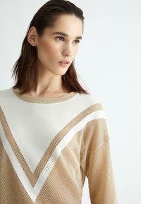 Maglione beige in rete con un motivo geometrico bianco e scollo rotondo. Texture morbida con una vestibilità ampia, che presenta un sottile dettaglio con logo.