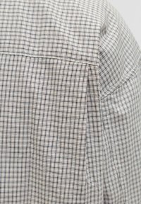 Trumpas rankovėmis marškiniai su šviesiai grietinėlės spalvos pagrindu, su mažomis tamsiai mėlynomis languotomis raštais. Minkšta medžiaga su sklandžiu tekstūros ir pritaikytais siūlais.