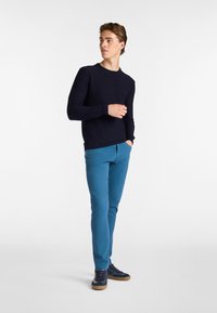 Marineblauer, gerippter Strickpullover, schmale, blaue Hose und dunkle Sneaker. Einfaches Design mit rundem Halsausschnitt und dezentem Logo auf der Brust.