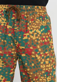 Herrshorts i ett flerfärgat, prickigt mönster med nyanser av brunt, grönt, gult och rött. Har midjeresår och dragsko.