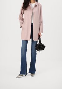 Light pink wool blend coat with a straight cut and open front. Paired with dark flared jeans and metallic pointed-toe shoes, holding a black bag.
