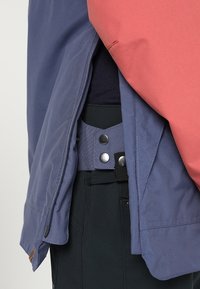 Lekka kurtka z niebieskim korpusem i koralowymi rękawami, z teksturowanym paskiem w talii i zapięciem na napy. Zamek błyskawiczny po boku.