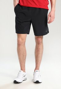 Schwarze Sportshorts mit elastischem Bund, die ein dezentes Nike-Logo tragen. Kombiniert mit weißen Sneakers und einem roten T-Shirt.