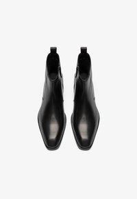 Botines de cuero negro con un diseño de punta afilada, que presentan cremalleras laterales y tiradores para ponérselos fácilmente. Textura suave y perfil elegante.