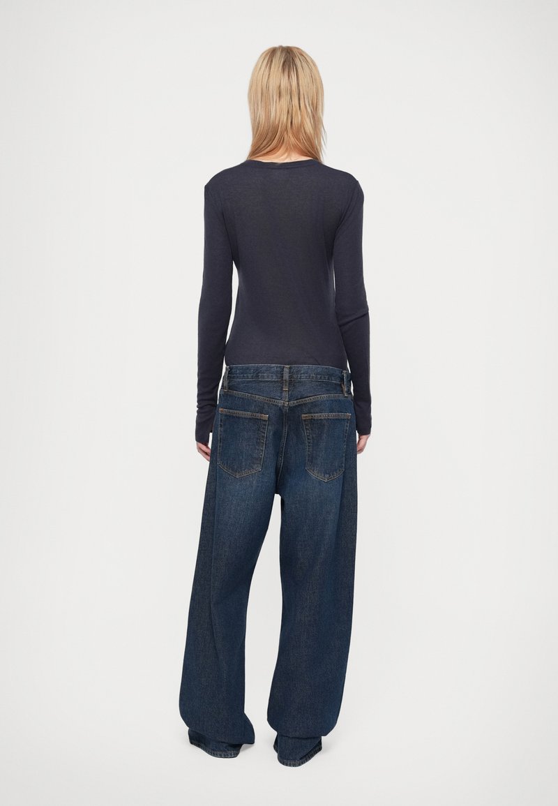 Dunkelbluse mit langen Ärmeln, kombiniert mit lockeren, weit geschnittenen blauen Jeans. Die Jeans haben Gesäßtaschen und ein klassisches Taillendesign.
