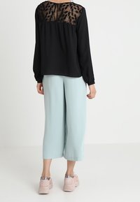 Sort langærmet bluse med gennemsigtig mønstret ryg, parret med lyseblå brede bukser og lyserøde sneakers.