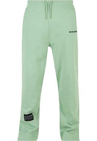 Hellgrüne Jogginghose aus weichem Stoff, mit einem elastischen Bund und Kordelzug sowie einem schwarzen Logo-Patch an der Seite.
