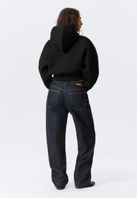 Μαύρο φούτερ με κουκούλα, κομμένο σχέδιο. Συνδυασμένο με σκουρόχρωμο τζιν φαρδύ σε ίσια γραμμή, με καφέ δερμάτινο έμπλαστρο και αντίθετες ραφές.