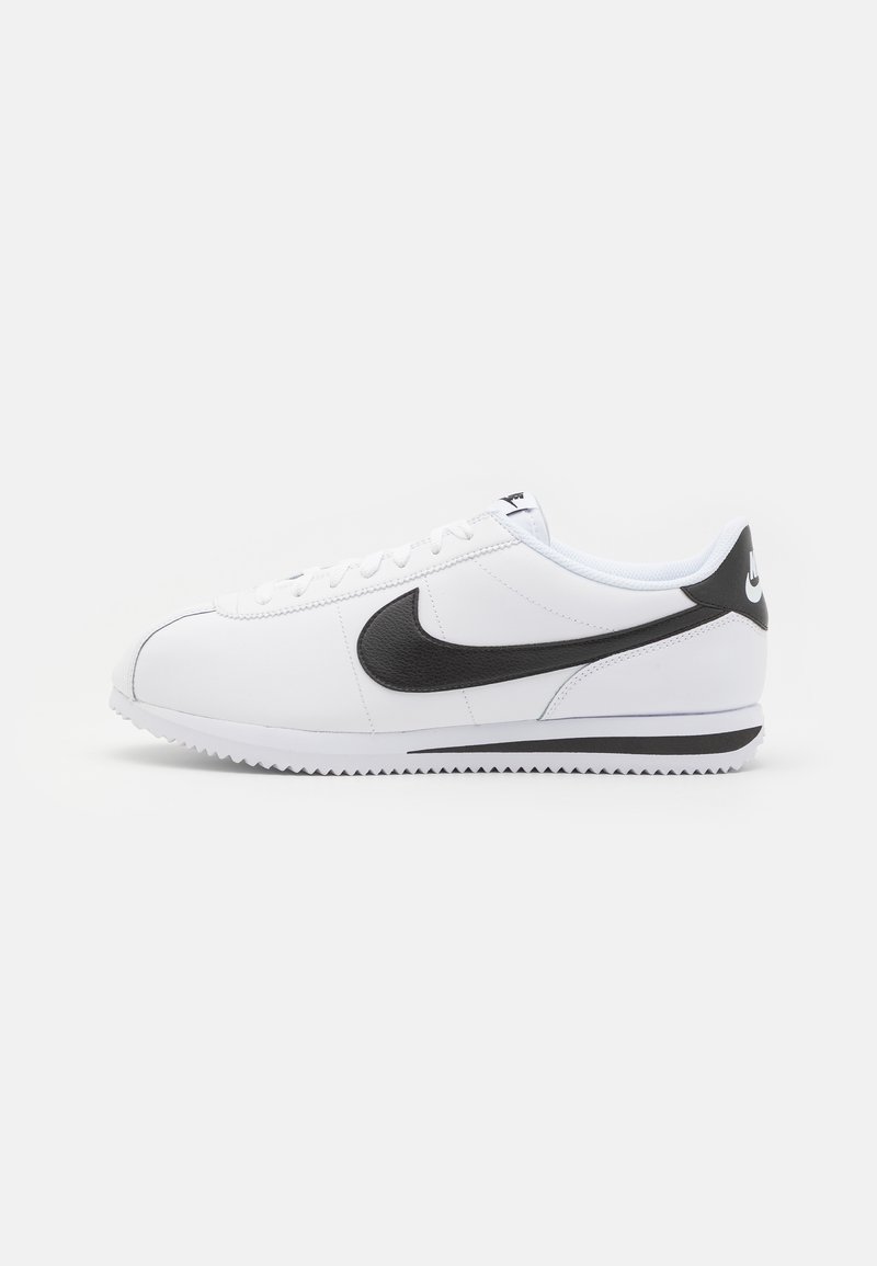 White leather sneakers with black Nike swoosh, flat laces, and textured rubber sole. Rounded toe and padded collar for comfort.