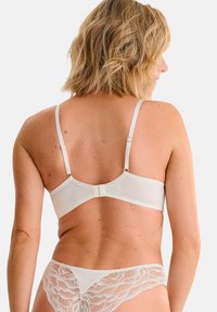 Ensemble de lingerie blanche comprenant un soutien-gorge lisse et simple avec des bretelles ajustables et une fermeture à crochets, associé à des culottes accentuées de dentelle avec des motifs floraux.