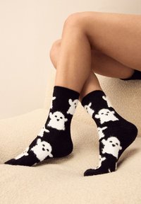 Zwarte sokken van zacht materiaal met een patroon van witte spookontwerpen. Enkelhoogte met een gezellige, zachte textuur.