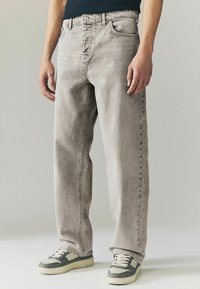 Lichtgrijze denim jeans met een recht model, voorzien van voorzakken, een knoopsluiting en subtiele textuur. Gemaakt in combinatie met sneakers met grijze accenten.