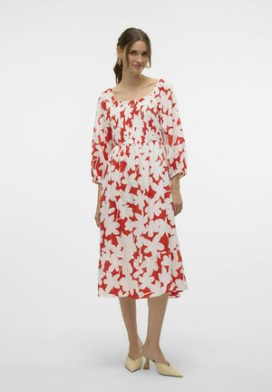 Vestido floral rojo y blanco con mangas largas, escote cuadrado, bodice fruncido y falda con volantes. Se muestra con mules beige.