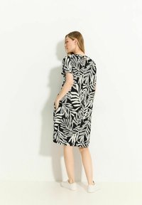 Schwarzes und weißes Kleid mit Blattmuster, kurzen Ärmeln, Seitentaschen und einem kleinen Schlüsselloch-Ausschnitt hinten. Lässiger Schnitt.
