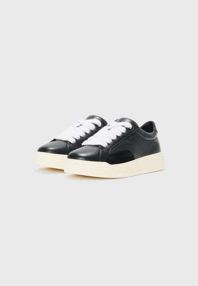 Black leather sneakers with white laces and a beige rubber sole. Rounded toe and a smooth texture, featuring subtle branding on the side.
