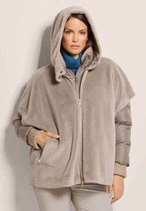 Beige fleece hooded jacket with a zip front, puffy gray sleeves, ribbed cuffs, and side pockets. Soft texture, oversized design.