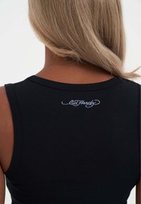 Sort ærmeløs top med en tætsiddende silhuet og en rund halsudskæring, samt et hvidt broderet logo på ryggen. Blødt, strækbart stof.