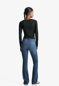 Svart långärmad topp kombinerad med blå flare jeans. Toppen har en figurnära design; jeansen har bakfickor och en lätt stretch.
