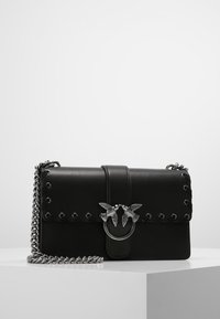 Černá kožená kabelka přes rameno se stříbrným řetízkovým popruhem a ozdobným stříbrným klasickým uzávěrem ve tvaru dvou ptáků čelící si navzájem.