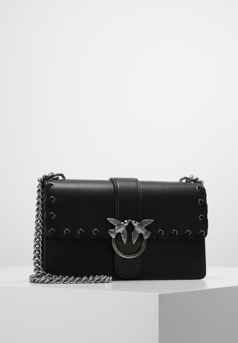 Černá kožená kabelka přes rameno se stříbrným řetízkovým popruhem a ozdobným stříbrným klasickým uzávěrem ve tvaru dvou ptáků čelící si navzájem.
