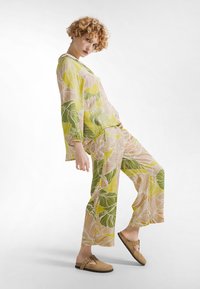 Conjunto con estampado floral que incluye una blusa suelta de manga larga y pantalones de pierna ancha en tonos verdes y amarillos, complementado con zapatos marrones tipo slip-on.