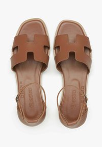 Bruine leren sandalen met uitsnijdingen, vierkante neus en verstelbare enkelriem. Gladde textuur met een platte, gewatteerde zool.