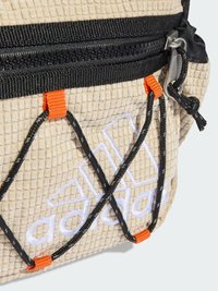 Šviesiai rudas tekstūruotas audinio krepšys su juodu užtrauktuku, oranžinėmis detalėmis ir išsiuvinėtu baltu logotipu. Pasižymi kryžminio bungee virvės dizainu.