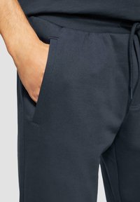 Marineblaue Baumwoll-Jogginghosen mit glatter Textur, elastischem Bund mit Kordelzug und seitlichen Taschen mit sauberen Kanten.