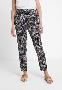 Námořnické kalhoty s béžovým listovým vzorem, s vysokým pasem, tapered střihem a bočními kapsami, v kombinaci se světlými sandály.