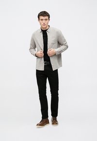 Svetlošedá košeľa na gombíky cez čierne tričko, v kombinácii s čiernymi nohavicami a hnedými šnurovacími topánkami. Minimalistický dizajn, jednofarebné.