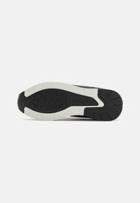 Semelle de sneaker noire avec des accents blancs. Comprend du caoutchouc texturé pour l'adhérence, des motifs circulaires en relief et un détail de marque bien visible.