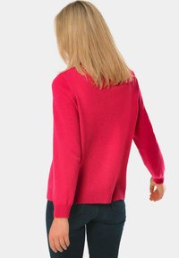 Fuchsia gebreide trui met lange mouwen, een ronde halslijn en geribbelde manchetten, gecombineerd met donkere spijkerbroeken. Zachte textuur en een ontspannen pasvorm.