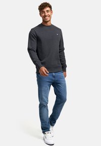 Dunkelgrauer Sweatshirt mit Rundhalsausschnitt und gerippten Bündchen, kombiniert mit hellblauen Jeans und weißen Turnschuhen. Einfaches Design, ohne Muster oder Akzente.
