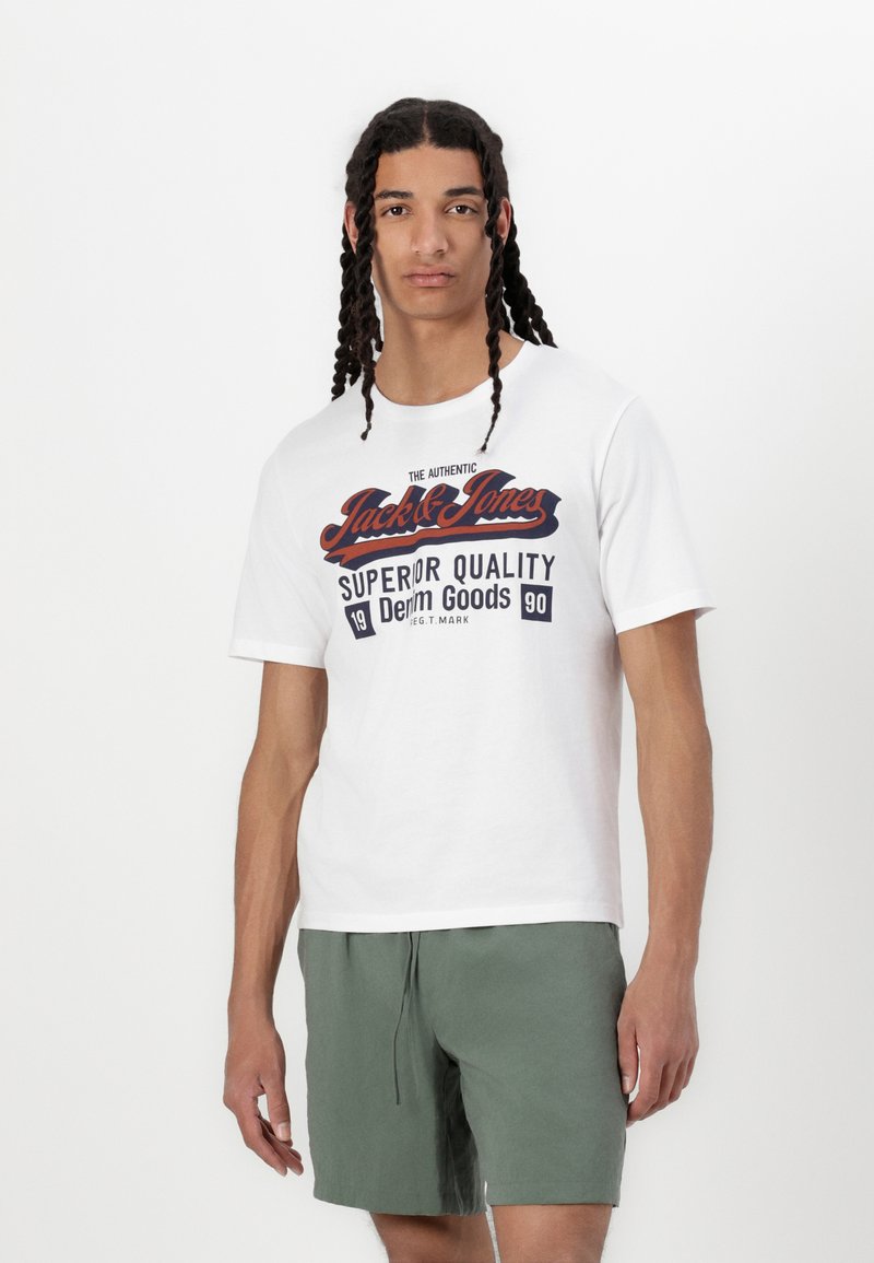 White cotton t-shirt with a crew neck, featuring a printed red and blue graphic text. Paired with light green shorts.