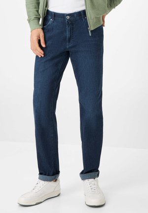 Dark blue denim jeans with straight cut, featuring a button and zipper closure, front pockets, and rolled cuffs. Worn with white sneakers.