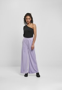 Zwarte één-schouder bodysuit gecombineerd met losse, lilac wijde broek. De broek heeft een elastische tailleband; outfit compleet met zwarte schoenen.