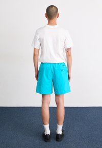 Herreoutfit bestående af en hvid T-shirt med rund hals og lyse turkise shorts. Shortsene har en elastisk talje og et lille logo-detalje.